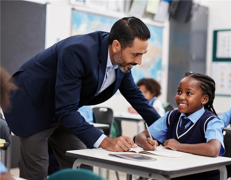 A teacher helps a pupil at their desk in a primary classroom.